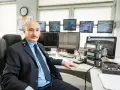 Mężczyzna w mundurze siedzi przy biurku z wieloma monitorami pokazującymi trasy kolejowe i urządzenia komunikacyjne.