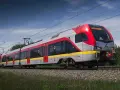 Nowoczesny pociąg do Łodzi mknie po torach wśród zieleni.