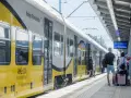 Pociąg Koleje Dolnośląskie na stacji. Ludzie z bagażami czekają na peronie, gotowi do podróży.