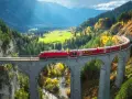 Czerwony pociąg Bernina Express przejeżdża przez kamienny wiadukt w górach jesienią.