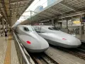 Dwa białe pociągi Shinkansen stojące na peronie, gotowe do podróży.