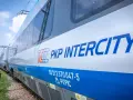 Pociąg PKP Intercity z niebieskim pasem i logo, na tle nieba.