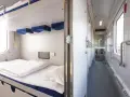 Wnętrze wagonu sypialnego z przygotowanym łóżkiem i korytarzem z drzwiami do przedziałów.