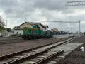 Zielona lokomotywa z pomarańczowymi pasami na torach. W tle budynki dworca i wagonów towarowych. Sprawdzam kętrzyn-olsztyn rozkład jazdy.
