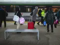 Ludzie z bagażami czekają na peronie PKP Intercity. Czerwona walizka stoi obok ławki.