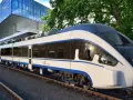 Nowoczesny, biało-niebieski pociąg Intercity ED161-002, najszybszy pociąg w Polsce, stoi na torach obok futurystycznego budynku.