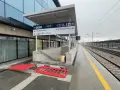 Nowoczesny dworzec kolejowy z tablicami kierunkowymi, peronami i torami w deszczu.