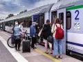 Ludzie z bagażami i rowerem czekają na pociąg PKP na peronie.
