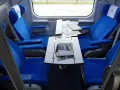 Wnętrze wagonu przedziałowego z wygodnymi, niebieskimi fotelami i stolikiem.