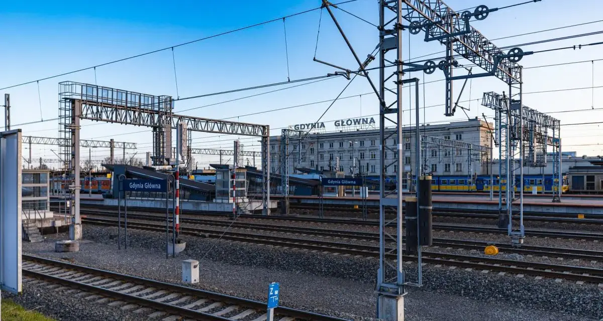 Stacja Gdynia Główna, początek lub koniec najdłuższej trasy kolejowej w Polsce. Tory, perony i budynek dworca pod błękitnym niebem.