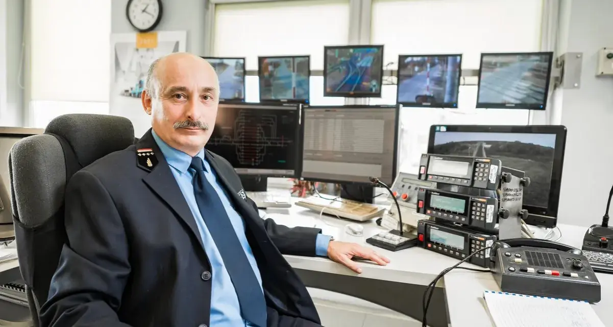 Mężczyzna w mundurze siedzi przy biurku z wieloma monitorami pokazującymi trasy kolejowe i urządzenia komunikacyjne.