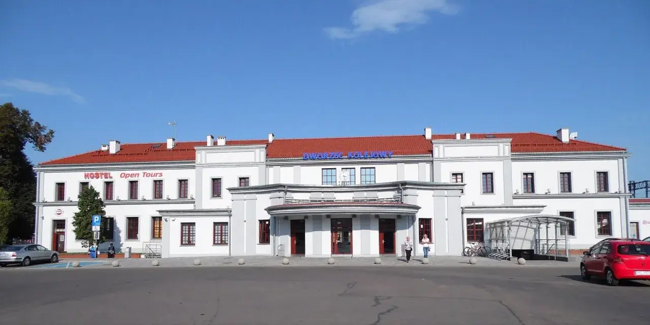 Dworzec PKP Ełk z czerwonym dachem i napisem "Dworzec Kolejowy". Obok hostel.