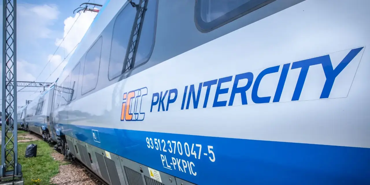 Pociąg PKP Intercity z niebieskim pasem i logo, na tle nieba.