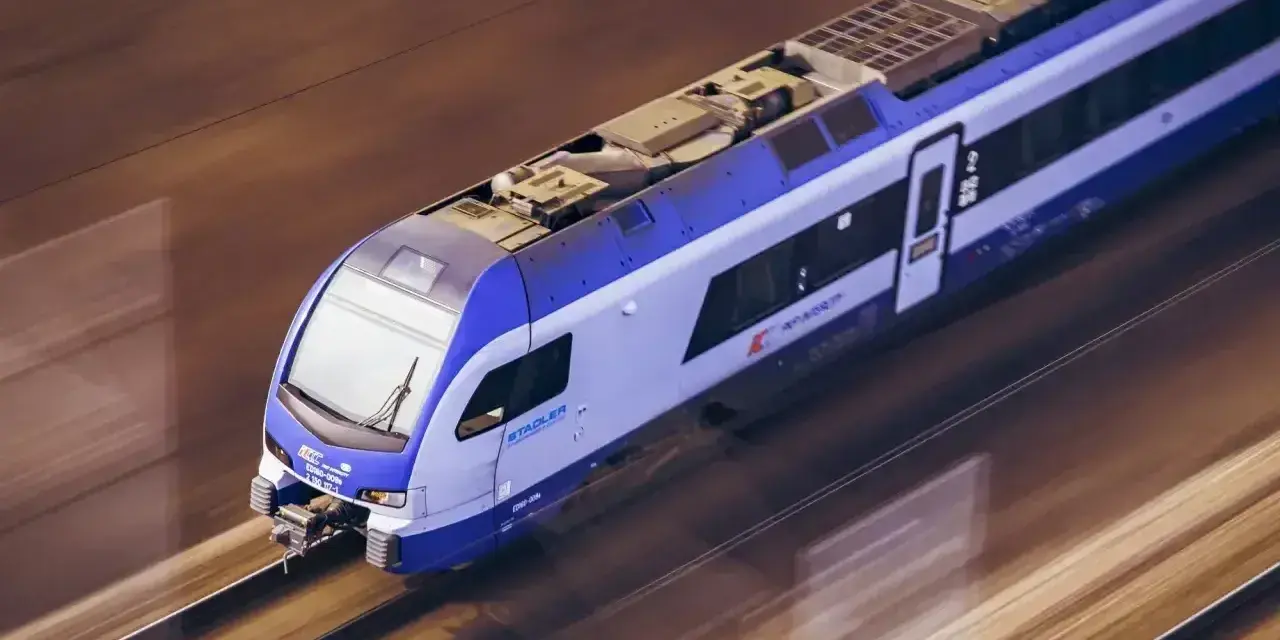Pędzący pociąg Stadler, pokonujący trasę Białystok - Lublin, mija rozmyte krajobrazy.