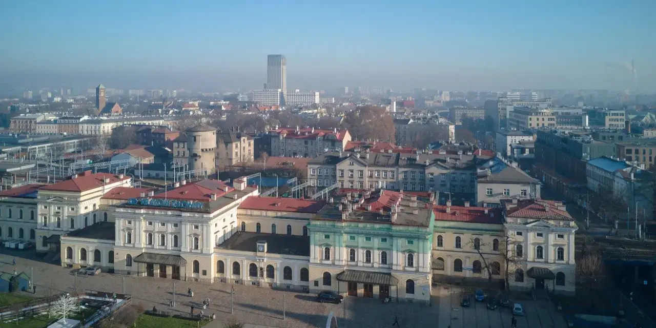 Widok na dworzec główny z tablicą "Kraków Główny". W tle miejska panorama.
