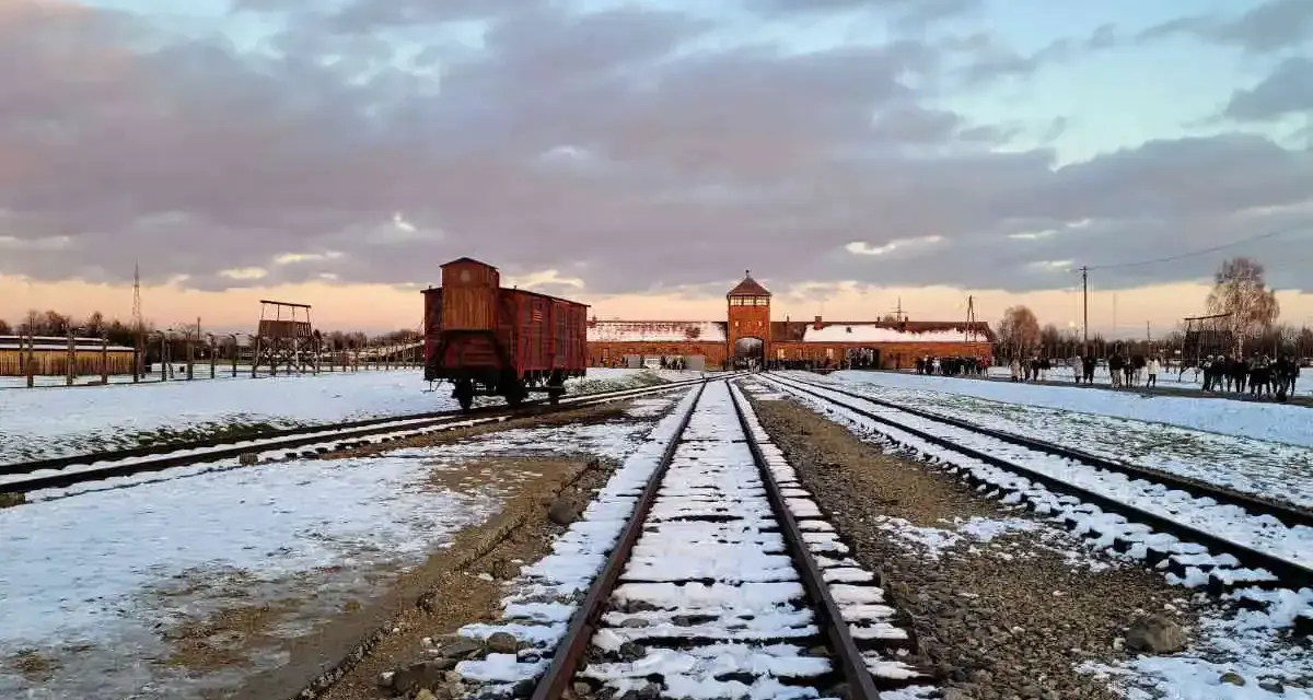 Zimowy krajobraz obozu Auschwitz z widocznym wagonem towarowym na torach, symbolem transportów do piekła.