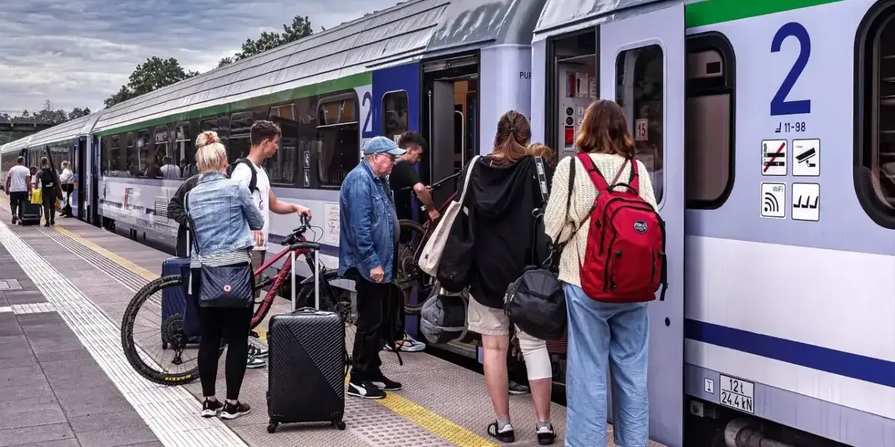 Ludzie z bagażami i rowerem czekają na pociąg PKP na peronie.