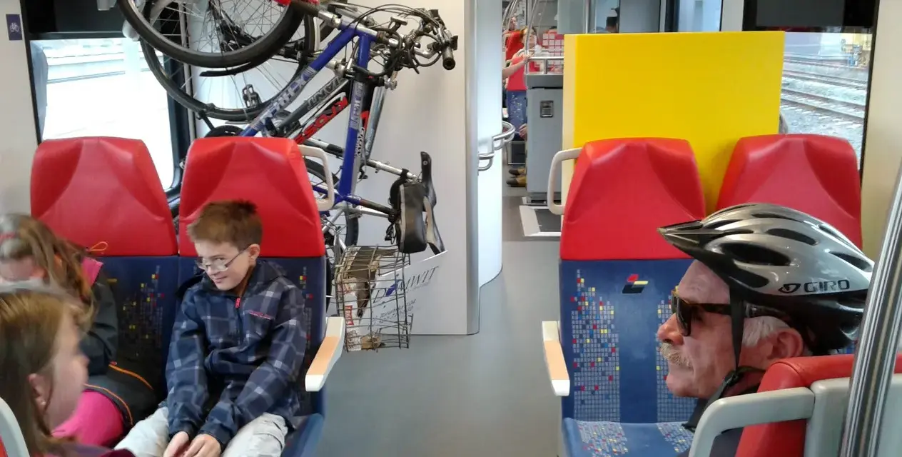 W pociągu Kolei Mazowieckich rowerzyści podróżują z rowerami. Dzieci i dorośli siedzą obok.