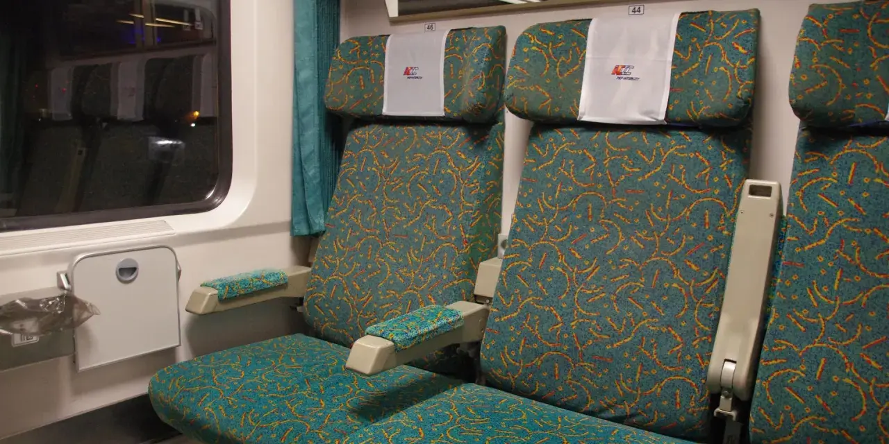 Wnętrze wagonu 4 Pendolino. Widok na dwa rzędy siedzeń z charakterystycznym wzorem.