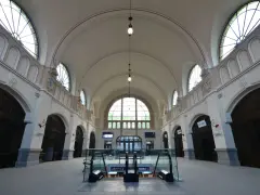 Wnętrze dworca kolejowego w Gdańsku z łukowymi oknami i schodami ruchomymi.