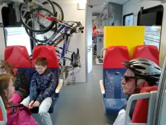 W pociągu Kolei Mazowieckich rowerzyści podróżują z rowerami. Dzieci i dorośli siedzą obok.