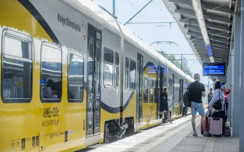 Pociąg Koleje Dolnośląskie na stacji. Ludzie z bagażami czekają na peronie, gotowi do podróży.