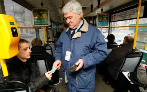 Kontroler biletów w niebieskiej kurtce sprawdza bilet młodego pasażera w autobusie.