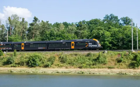 Czarny pociąg Leo Express z pomarańczowymi akcentami jedzie wzdłuż zielonego brzegu. Szukasz tanich biletów PKP Warszawa - Kraków?