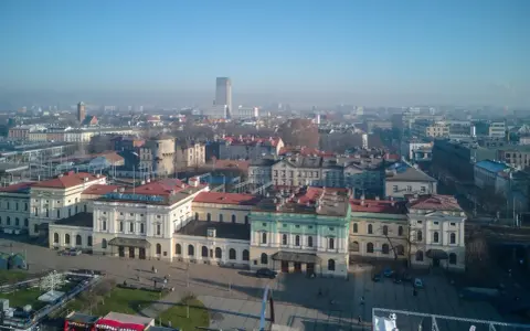 Widok na dworzec główny z tablicą "Kraków Główny". W tle miejska panorama.
