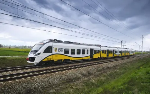 Pociąg Kolei Dolnośląskich z charakterystycznym żółto-białym malowaniem jedzie po torach. Zniżki dla żołnierzy zawodowych PKP to świetna okazja do podróżowania.