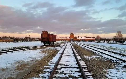 Zimowy krajobraz obozu Auschwitz z widocznym wagonem towarowym na torach, symbolem transportów do piekła.