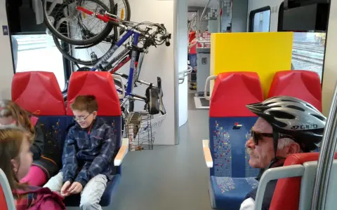 W pociągu Kolei Mazowieckich rowerzyści podróżują z rowerami. Dzieci i dorośli siedzą obok.