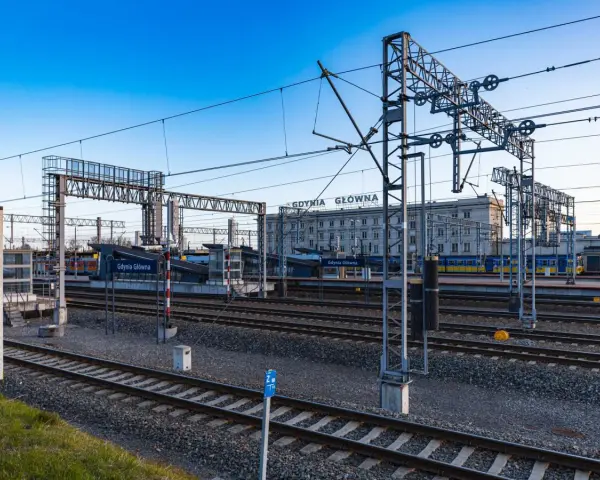 Stacja Gdynia Główna, początek lub koniec najdłuższej trasy kolejowej w Polsce. Tory, perony i budynek dworca pod błękitnym niebem.
