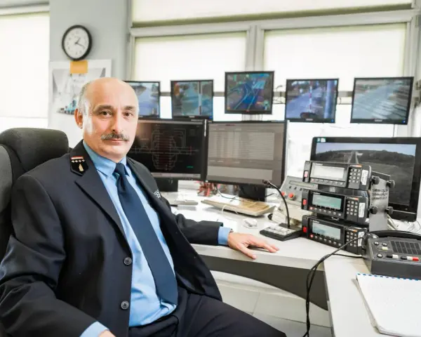 Mężczyzna w mundurze siedzi przy biurku z wieloma monitorami pokazującymi trasy kolejowe i urządzenia komunikacyjne.