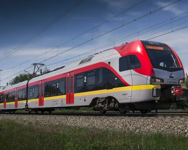 Nowoczesny pociąg do Łodzi mknie po torach wśród zieleni.