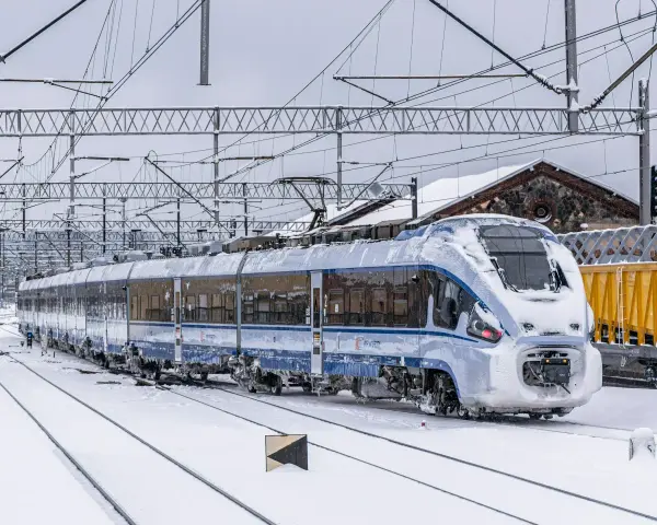 Pociąg PKP Intercity pokryty lodem i śniegiem, stojący na zaśnieżonych torach. Utrudnienia w ruchu kolejowym z powodu zimy.