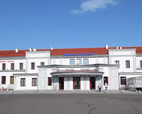Dworzec PKP Ełk z czerwonym dachem i napisem "Dworzec Kolejowy". Obok hostel.
