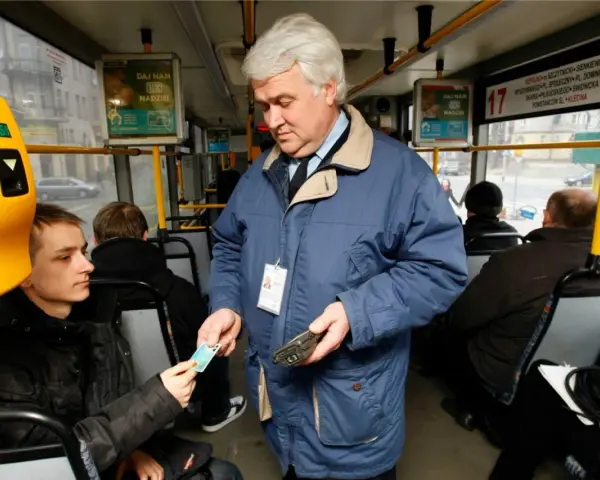 Kontroler biletów w niebieskiej kurtce sprawdza bilet młodego pasażera w autobusie.