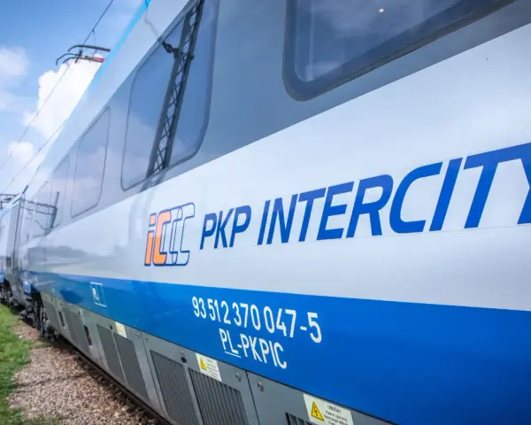 Pociąg PKP Intercity z niebieskim pasem i logo, na tle nieba.
