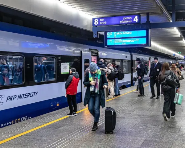 Ludzie na peronie PKP Intercity, gotowi do podróży. Może ktoś właśnie sprawdza, czy dopłata do biletu ulgowego PKP jest konieczna.