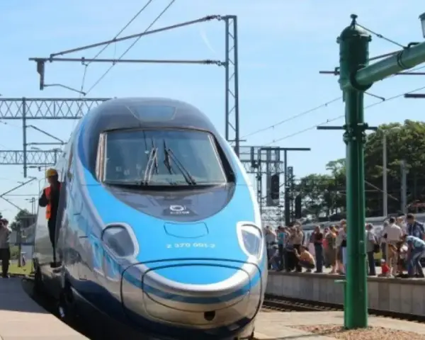 Błękitno-szary pociąg Pendolino na peronie, ludzie czekają na podróż. Oznaczenie Pendolino w rozkładzie jazdy.