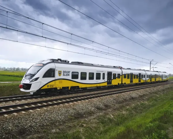 Pociąg Kolei Dolnośląskich z charakterystycznym żółto-białym malowaniem jedzie po torach. Zniżki dla żołnierzy zawodowych PKP to świetna okazja do podróżowania.