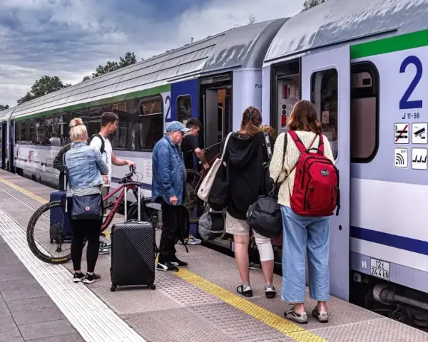Ludzie z bagażami i rowerem czekają na pociąg PKP na peronie.