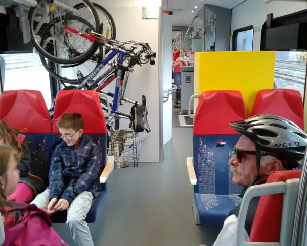 W pociągu Kolei Mazowieckich rowerzyści podróżują z rowerami. Dzieci i dorośli siedzą obok.