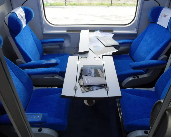 Wnętrze wagonu przedziałowego z wygodnymi, niebieskimi fotelami i stolikiem.