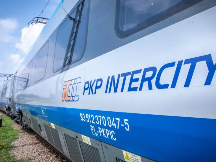 Pociąg PKP Intercity z niebieskim pasem i logo, na tle nieba.