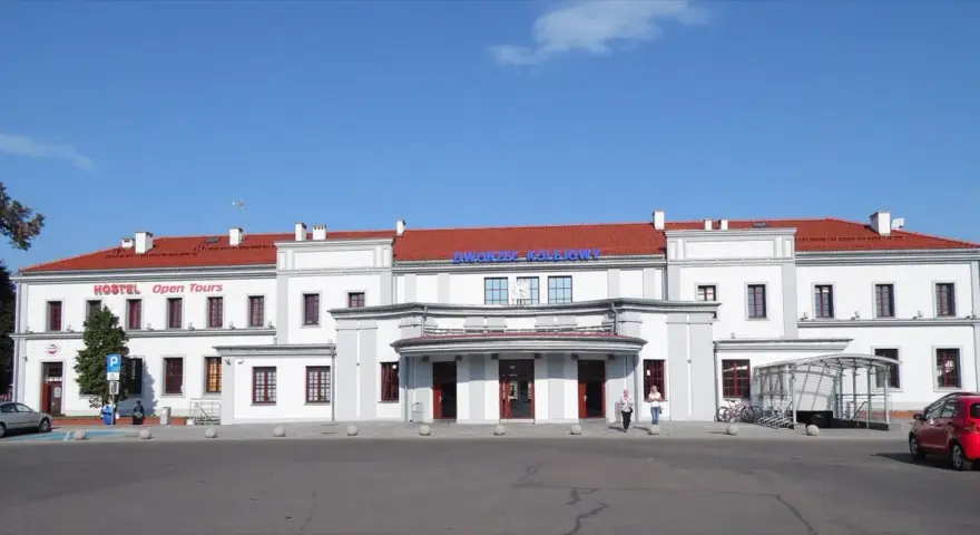 Dworzec PKP Ełk z czerwonym dachem i napisem "Dworzec Kolejowy". Obok hostel.