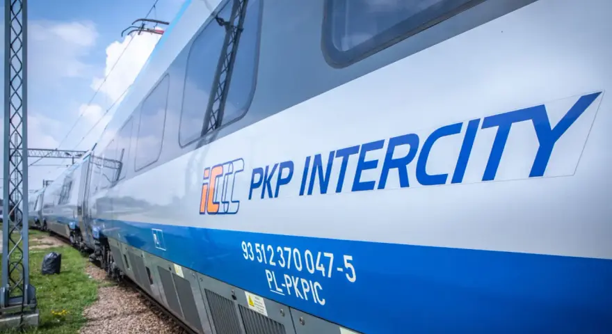 Pociąg PKP Intercity z niebieskim pasem i logo, na tle nieba.