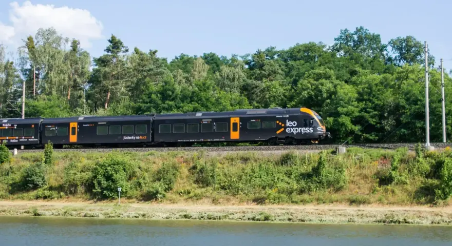 Czarny pociąg Leo Express z pomarańczowymi akcentami jedzie wzdłuż zielonego brzegu. Szukasz tanich biletów PKP Warszawa - Kraków?