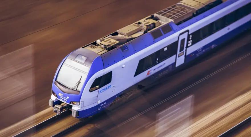 Pędzący pociąg TLK Flisak, którego rozkład jazdy jest kluczowy dla podróżnych, mija krajobraz w rozmytych barwach.